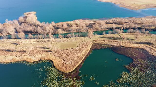 Long peninsula or island and a river in the middle - landform caused by sediment deposition where stream Ljuca flows into lake Plav water in Montenegro. Aerial drone view of promontory on a sunny day.