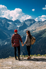 Fototapeta na wymiar A couple in love on a rock admires the beautiful views. A man and a woman on a rock. A couple in love travels. A man and a woman in the Caucasus mountains. Couple traveling through the mountains