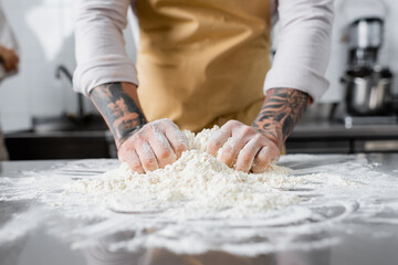 Cropped view of tattooed chef making dough near blurred flour in kitchen