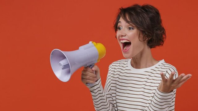 Excited vivid promoter young brunette woman 20s wears striped shirt point index finger aside scream in megaphone announces discounts sale Hurry up isolated on plain orange background studio portrait