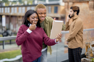 Black students having video call on digital tablet outdoors. Concept of remote and e-learning. Idea of students lifestyle. Smiling young girl and guy. Man waving hand. University campus