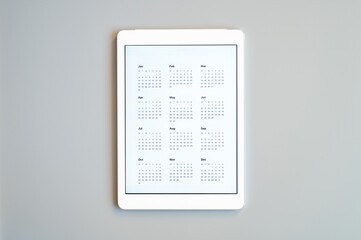 tablet computer with an open app of calendar for unspecified unknown date year without date on a gray background. concept business or to do list goals with technology using. top view, flat lay