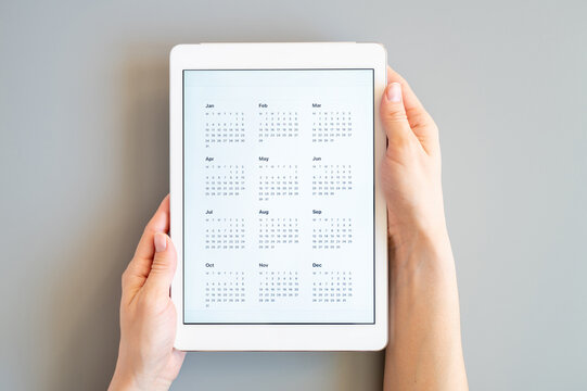 tablet computer with an open app of calendar for unspecified unknown date year without date in a womans hands on a gray background. concept business or to do list goals. top view, flat lay