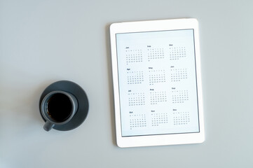 tablet computer with an open app of calendar for unspecified unknown date year without date and cup of tea or coffee on a gray background. concept business or to do list goals. top view, flat lay