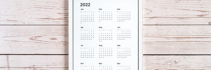 tablet computer with an open app of calendar for 2022 year on a wooden boards background. concept business or to do list goals with technology using. top view, flat lay. banner