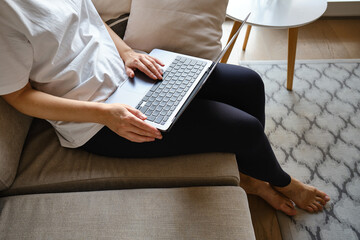 Girl works on the laptop on the couch at home or in hotels. Remote work. Office at home. Woman in the bedroom is typing on a laptop, distance learning for students, surfing the Internet