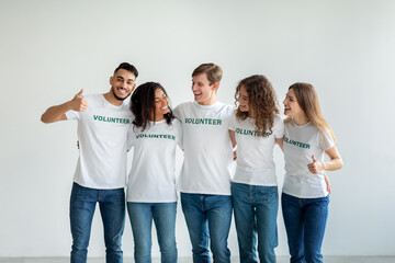 Fototapeta premium Young multiracial volunteers embracing and having fun over light studio wall, smiling and posing