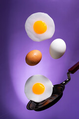 whole and fried eggs above a frying pan float in the air on a violet. Breakfast time