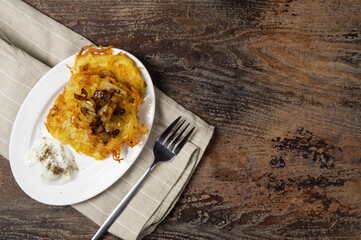 Potato pancakes with fried onions and sour cream served on wooden table