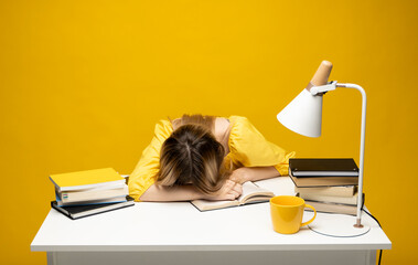 Student studying exam and sleeping on books on a yellow background. Tired student girl with glasses sleeping on the books in the library.