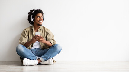 Cheerful Black Guy Using Smartphone And Wireless Headphones For Listening Music Online