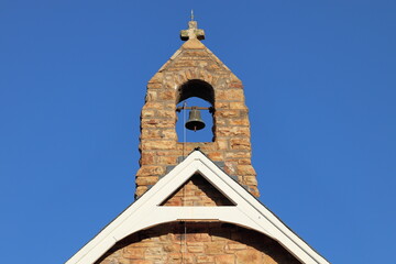 Fototapeta na wymiar Sandstone bell tower of small chapel with blue sky. Architecture, religion, history, travel concept. Copy space.