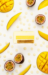 Top view of delicious mango and passion fruit mousse cake slice with the layers displayed and recipe ingredients arranged over white background. Restaurant menu and confectionery concept in flat lay