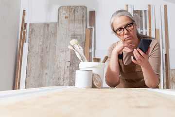 wood crafts, woman artisan carpenter with mobile phone search the internet in her workshop, restoration, diy and handmade works concept