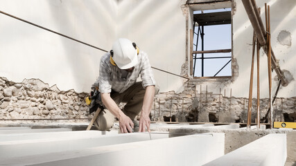 man at work, construction worker wear a helmet, check the measurements and distances of the beams at the base of the foundations of the second floor of house, in renovation building site background