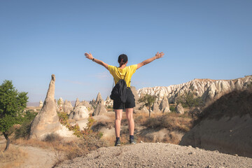 Woman tourist standing back with raised hands on turkish mountains background in Cappadocia