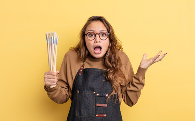 hispanic pretty woman feeling extremely shocked and surprised. artist with brushes concept