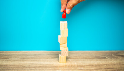 Hand put red pin to the brown cubic stack on the table and blue background with copy space