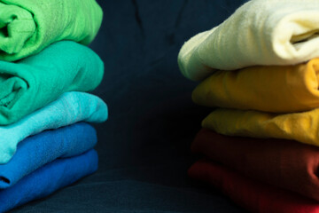 Stacks of multicolored fabrics in cool and warm colors are compared next to each other. Background with folded clothes with blank space for information. T-shirts of different colors