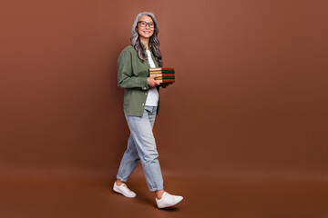 Fototapeta na wymiar Full size photo of nice old white hairdo lady hold books go wear shirt eyesight jeans footwear isolated on brown color background