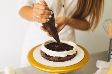 Confectioner girl is preparing a cake biscuit with white cream and chocolate. Concept ingredients for cooking flour products or dessert. Rural or rustic style.