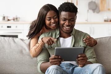 Cheerful african american couple having fun at home, using pad