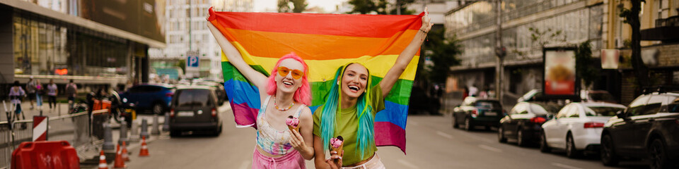 Young lesbian couple eating ice cream while walking with rainbow