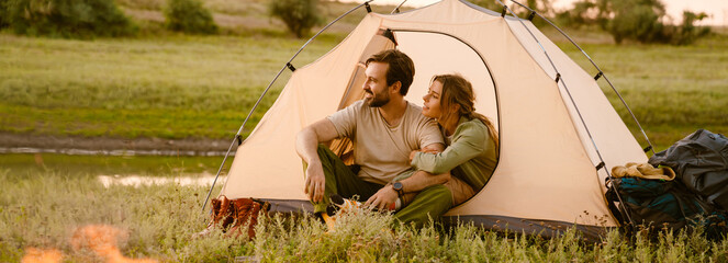 White couple hugging and sitting in tent during camping together - obrazy, fototapety, plakaty