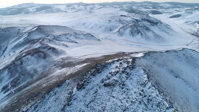 Aerial forward Epic winter snow-covered mountain tundra Buryatia, Siberia abstract natural landscape. Roads through wild untouched terrain, off-road. Hills shaman's way. Reserve. Open space, horizon