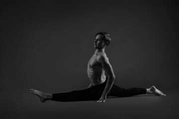 Black and white portrait athletic man performs a split exercise on a dark background.