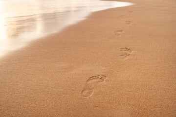 Footprints on the white sand of the beach along the wave. Summer vacation concept. Background for your design witn copy space.