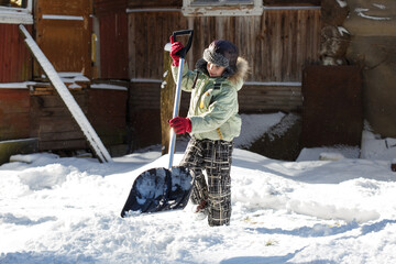 Little boy helps to shovel snow on a clear winter day in the countryside.