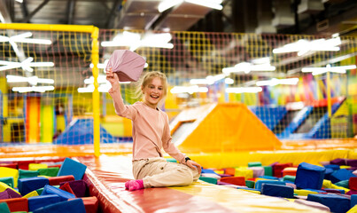 Pretty girl kid sitting on colorful trampoline at playground park and holding gum cube. Beautiful female child happy during active entertaiments indoor