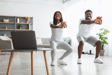 Young black couple doing squats exercise in front of laptop