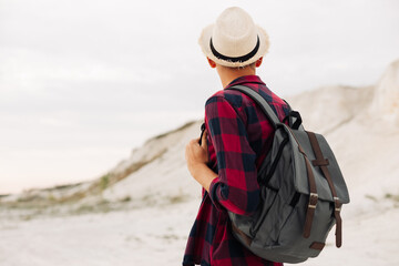 Male hipster traveler with backpack in hat looking forward to amazing mountains and valleys view