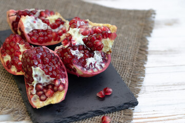 pomegranate fruit open on black slate board, side view, light vintage wooden background.