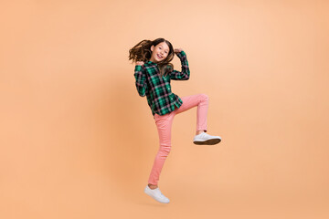 Photo of funny lucky school girl dressed checkered clothes smiling humping high rising fists isolated beige color background