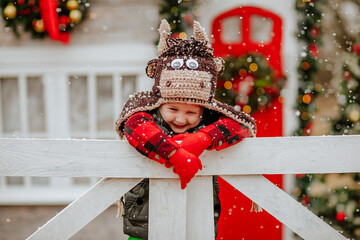 Boy in bull hat and red gloves posing up white fence and making funny faces