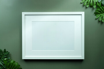 Blank picture frame and green monstera leaf on green background.