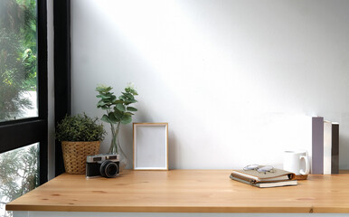 Creative workspace with blank poster frame, camera, coffee cup and houseplant on wood table..