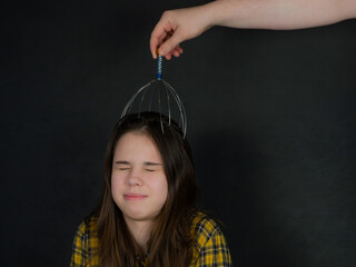 Metal instrument for head massage. A teenage girl is given a head massage with a capillary...