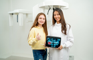 Asian dentist woman stand with young girl in front of dental x-ray machine.