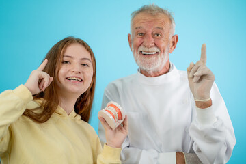 Senior dentist hold big model of teeth while young girl hold small one and they look fun action on blue background