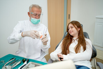 Senior dentist try to entertain and talk with young girl to relax during treatment process in dental clinic.