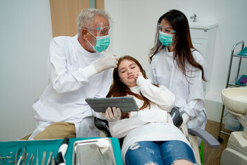 Lovely girl lie on dental clinic chair and wait for treatment during senior dentist discuss with staff.