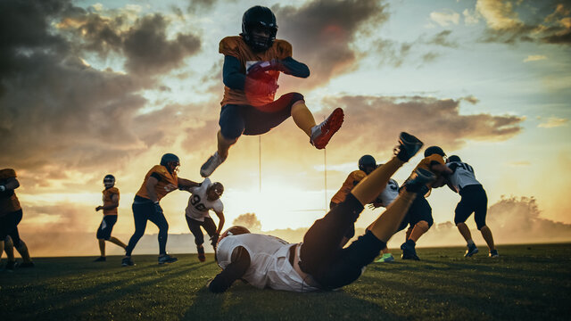 American Football Field Start of Offensive Play with a Snap Pass: Successful Player Jumping Over Defense Running to Score Touchdown Points. Professional Athletes Compete Fight for Victory
