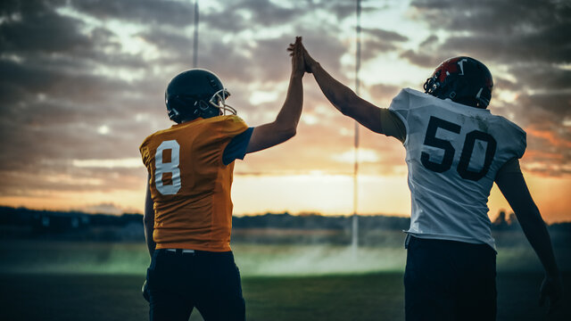 American Football Game Start Teams Ready: Two Professional Players Walk On Field Determined To Win The Match. Competitive Friends Do Celebration High-Five. Back View Shot