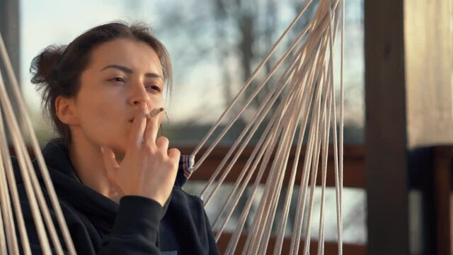 Portrait of a beautiful young woman smoking a cigarette in the evening on the veranda. Close-up of a thoughtful face of a girl looking into the distance in the open air.