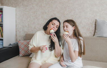 Obraz na płótnie Canvas happy mom and daughter eating delicious strawberry shortcake sitting at home on the couch