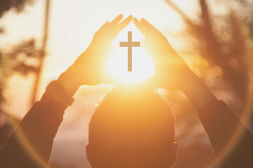 View of cross in light of sun through silhouette of human hands. Close up.